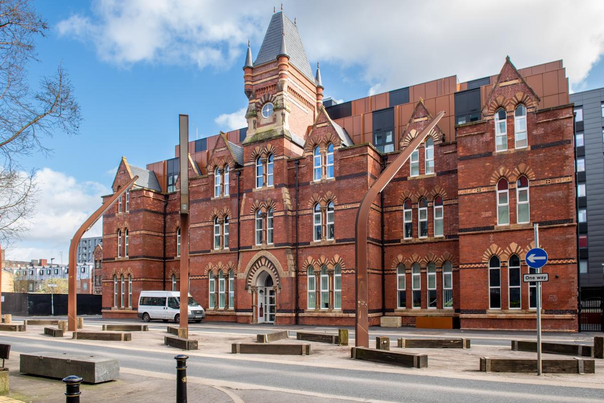 External photo of Ancoats Dispensary building with a bold red brick facade and clock tower. 