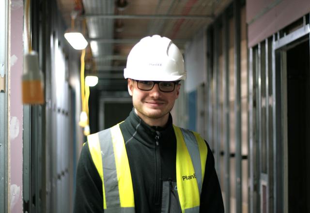 Man smiling at the camera standing inside a construction site. 