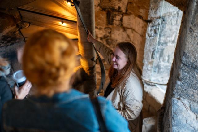 a lady smiles up in conversation with others on a stone spiral staircase at caernarfon castle