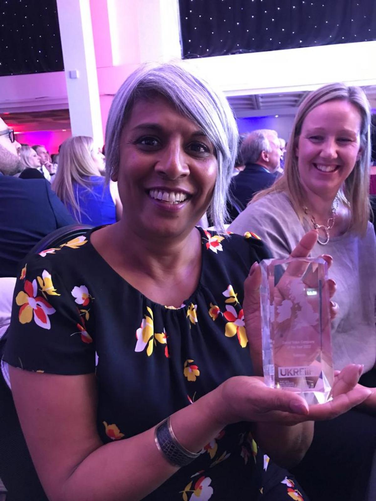 chithra posing and smiling at ukreiif event holding glass award under purple lighting 