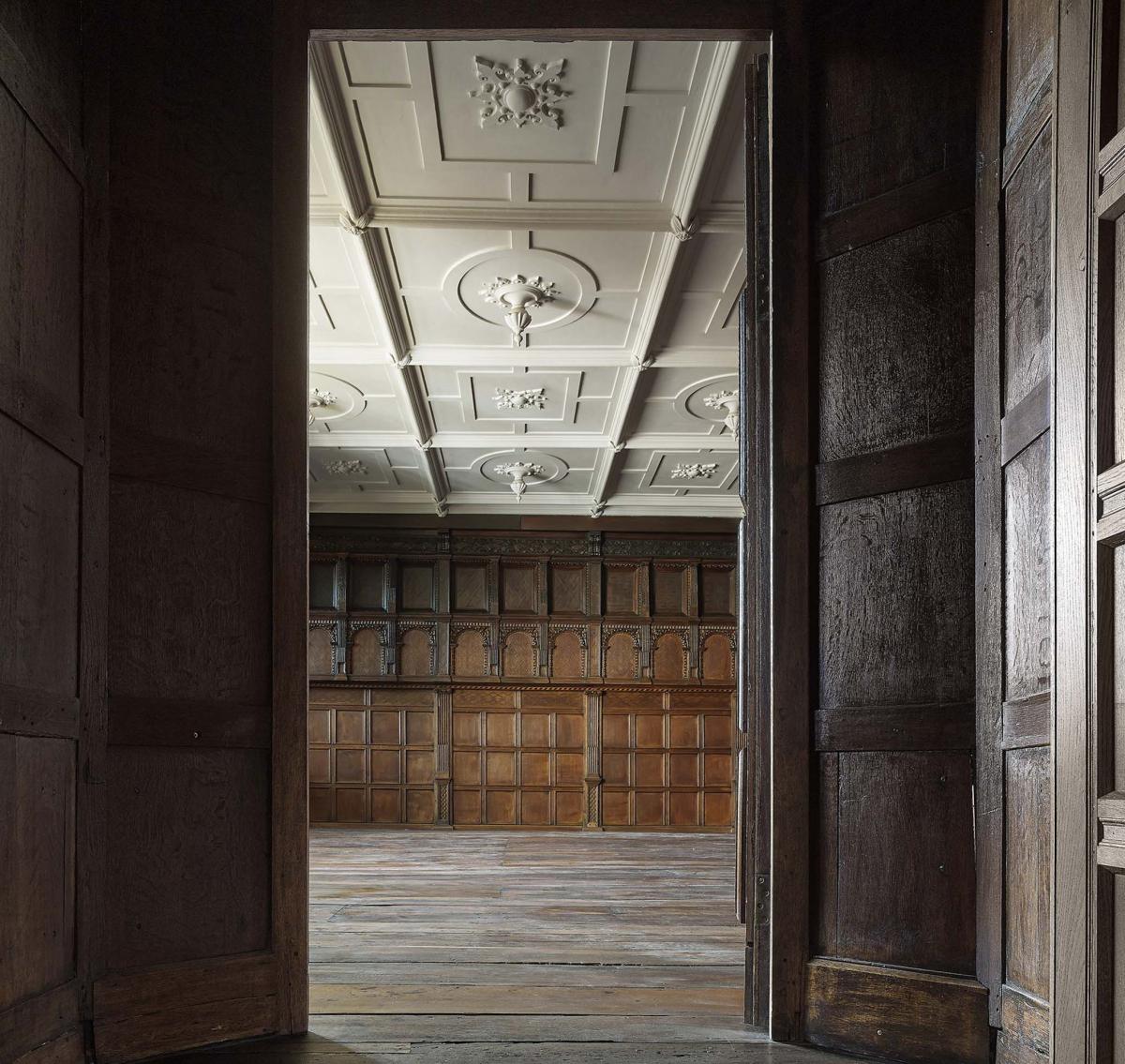 interior of wythenshawe hall withdrawing room after restoration with intricate white ceiling and dark wooden walls and floors