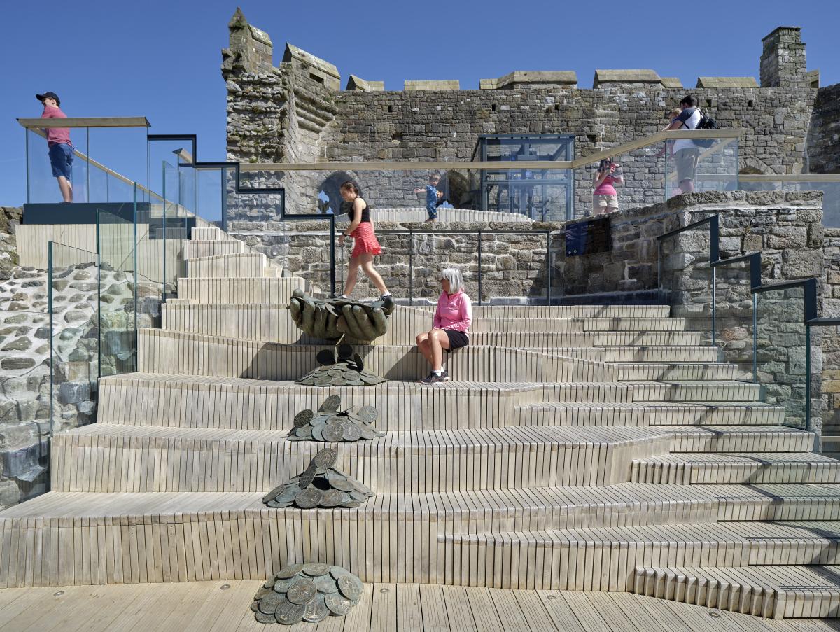 People sitting on the tiered timber seating, on the upper deck of Caernarfon Castle