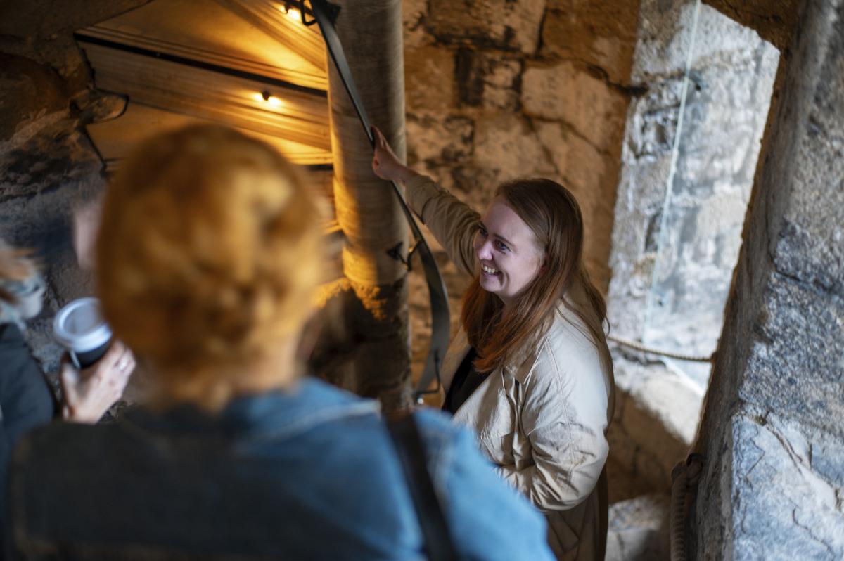 Two ladies stand at the base of a spiral stair smiling and talking to one another.