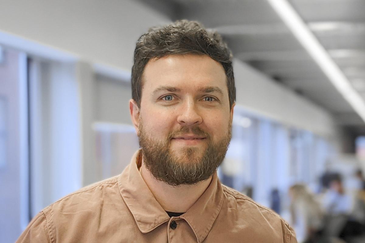 Headshot of Paul Wright, a man with brown hair and a beard wearing a brown shirt.