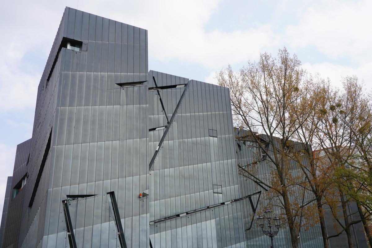 Very angular grey building in three cuboid parts sloping down a hill.