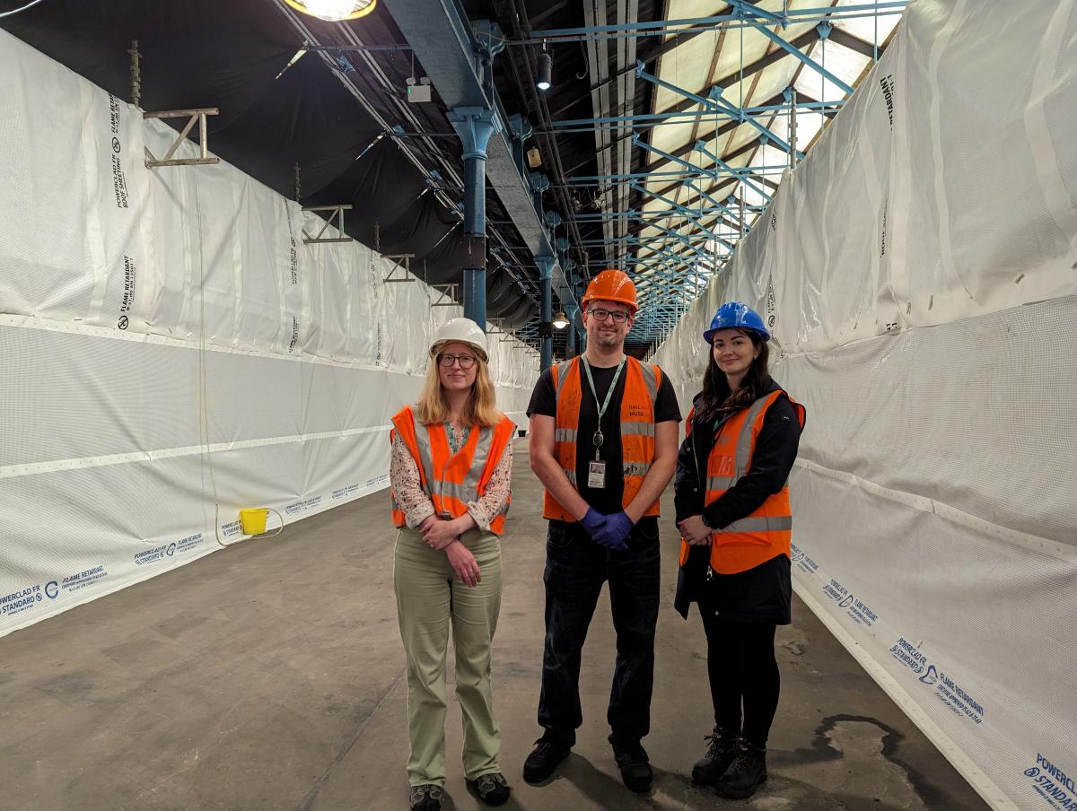 Three people standing in front of two poly tunnels which are the protective shields for the collection.