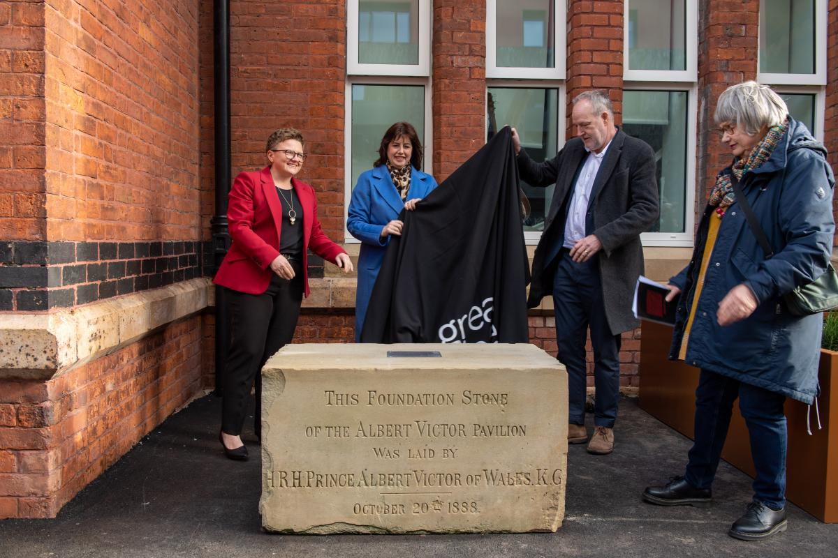 External photograph of four people unveiling a large sandstone foundation stone with inscription on it from 1888 