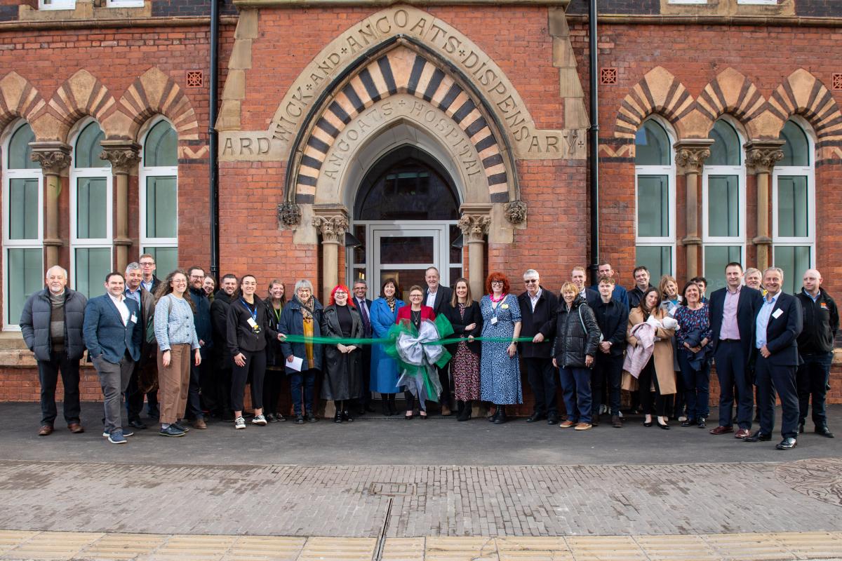 A large group of people stand infront of the main entrance of Ancoats Dispensary. 