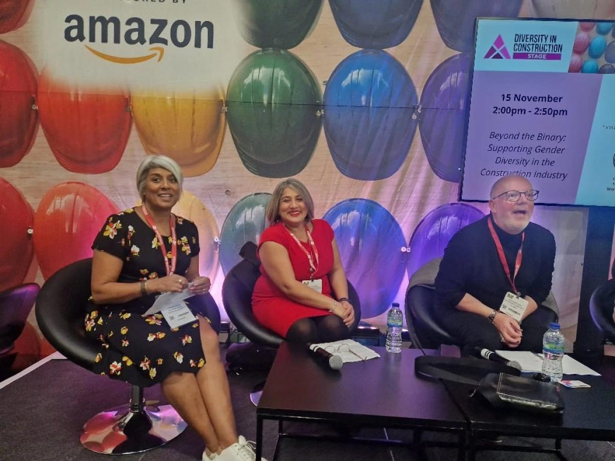 Three people sitting at a low table in their hands are scripts for their presentations. Behind them is a screen with the word 'Amazon' written on it. 