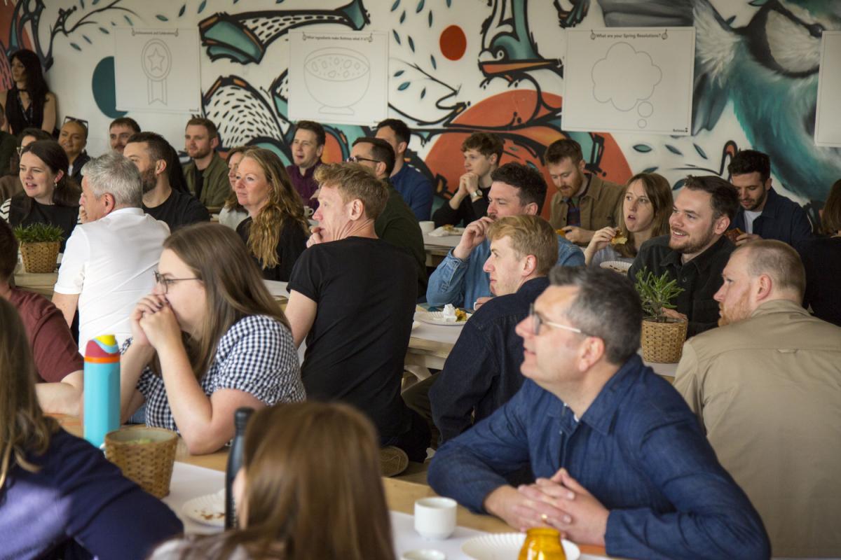 a group of people are turned towards a speaker. they are in a room with graffiti murals on the walls.