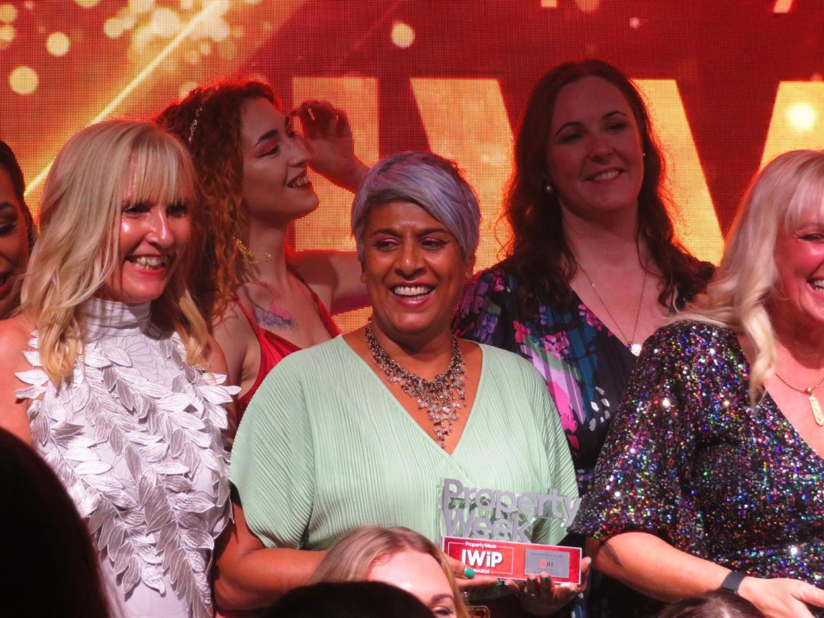 Image of women standing to receive applause at the end of an awards event. Chithra is centre in the image, smiling and holding her award. 