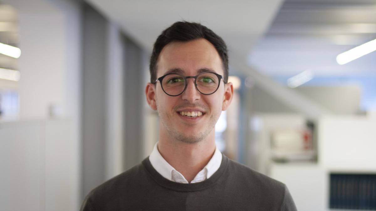 Headshot of Cameron Hawkins, a man with dark hair and glasses smiling at the camera