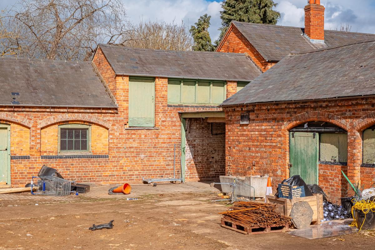 Delapre Abbey Stables pre-construction. Orange brick one-storey building with green doors.