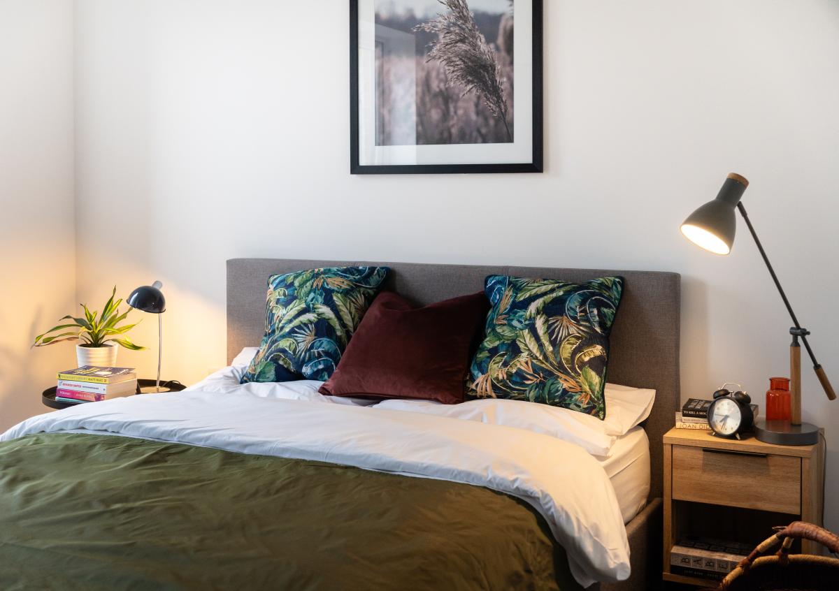 Internal image of a bedroom with a double bed with green bed linen. Each side of the bed has a small side table and lamp. 