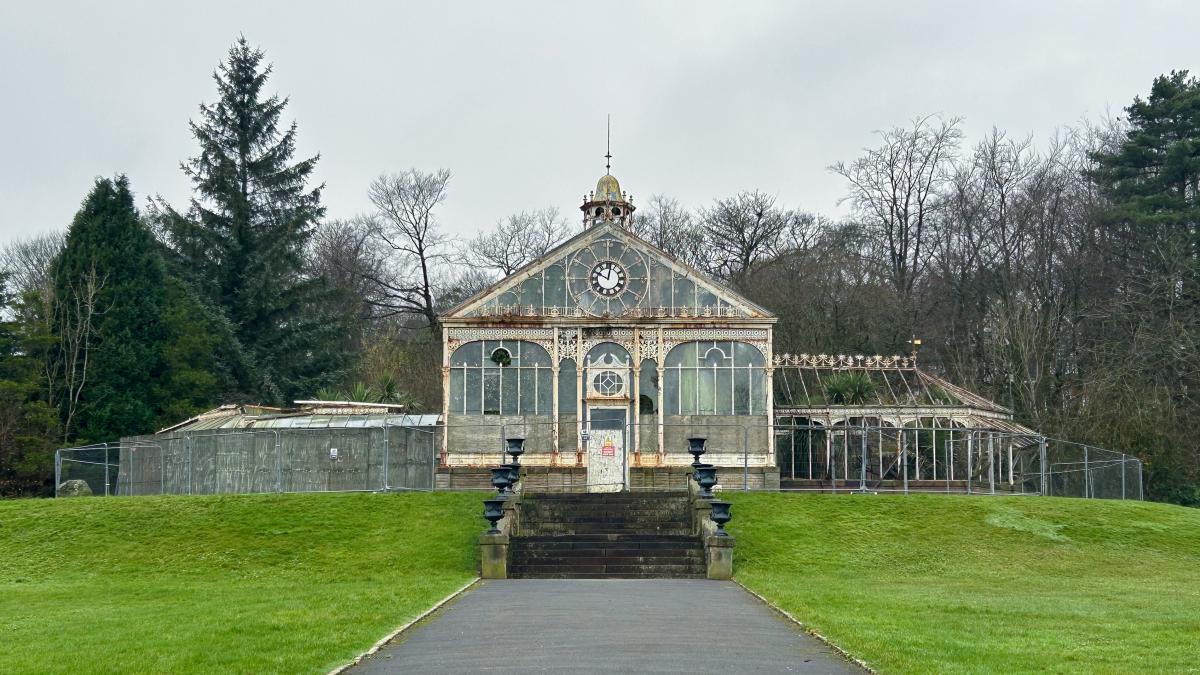 Blackburn Conservatory - a glass and white wood greenhouse style building on grass with trees behind.