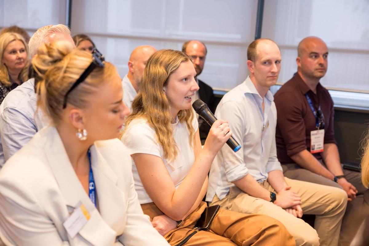 Four people sat in an audience of an event. One of the women is holding a microphone.