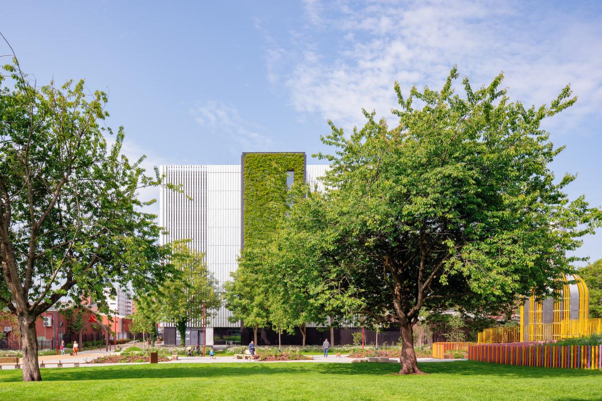 Modern building with vertical garden behind a green park with trees and a colourful playground.
