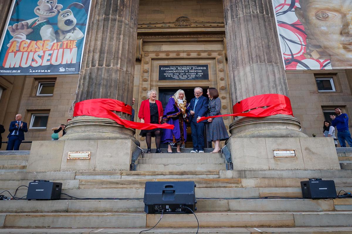 Exterior of the Harris Museum with three people stood on the steps cutting the red ribbon.