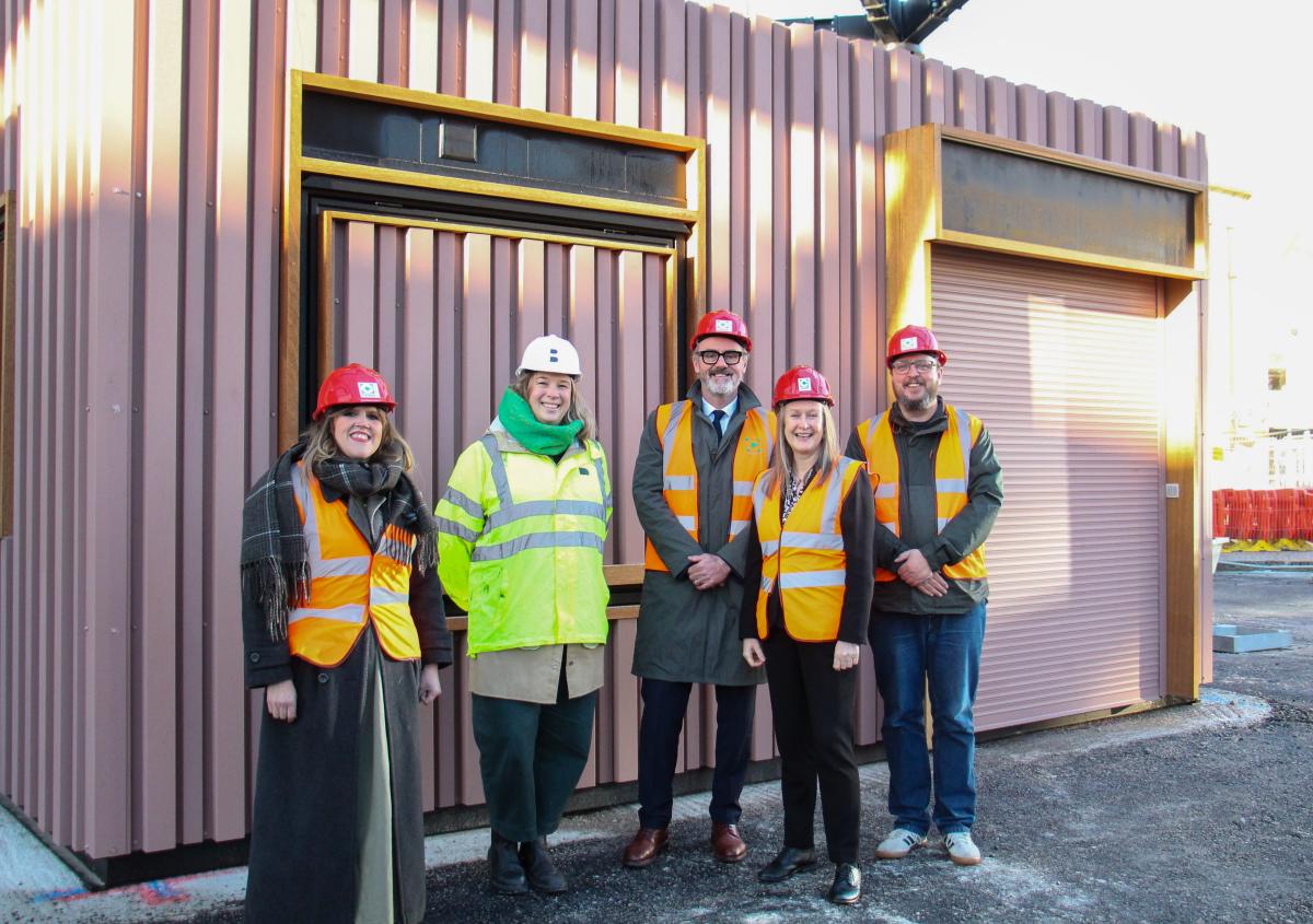 Five people wearing high vis vests and hard hats standing in front of a kiosk.