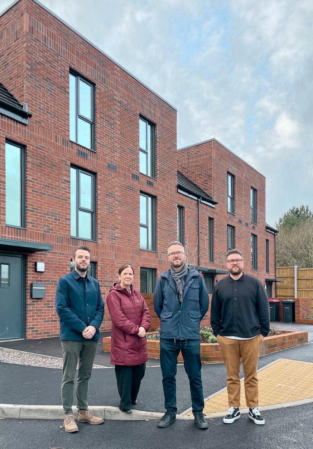 Four people standing outside a red brick house