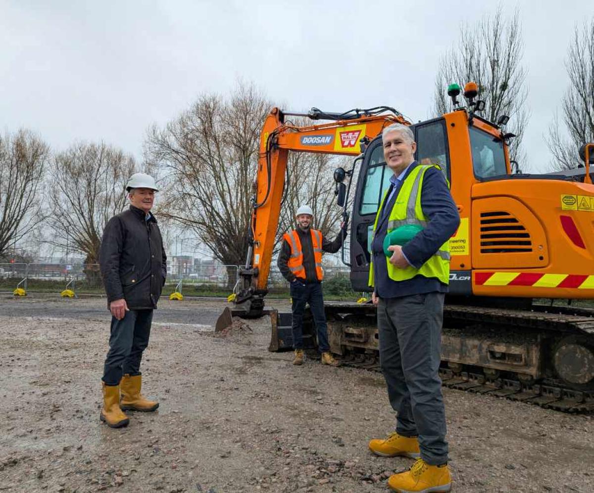 Three men standing in front of orange digger