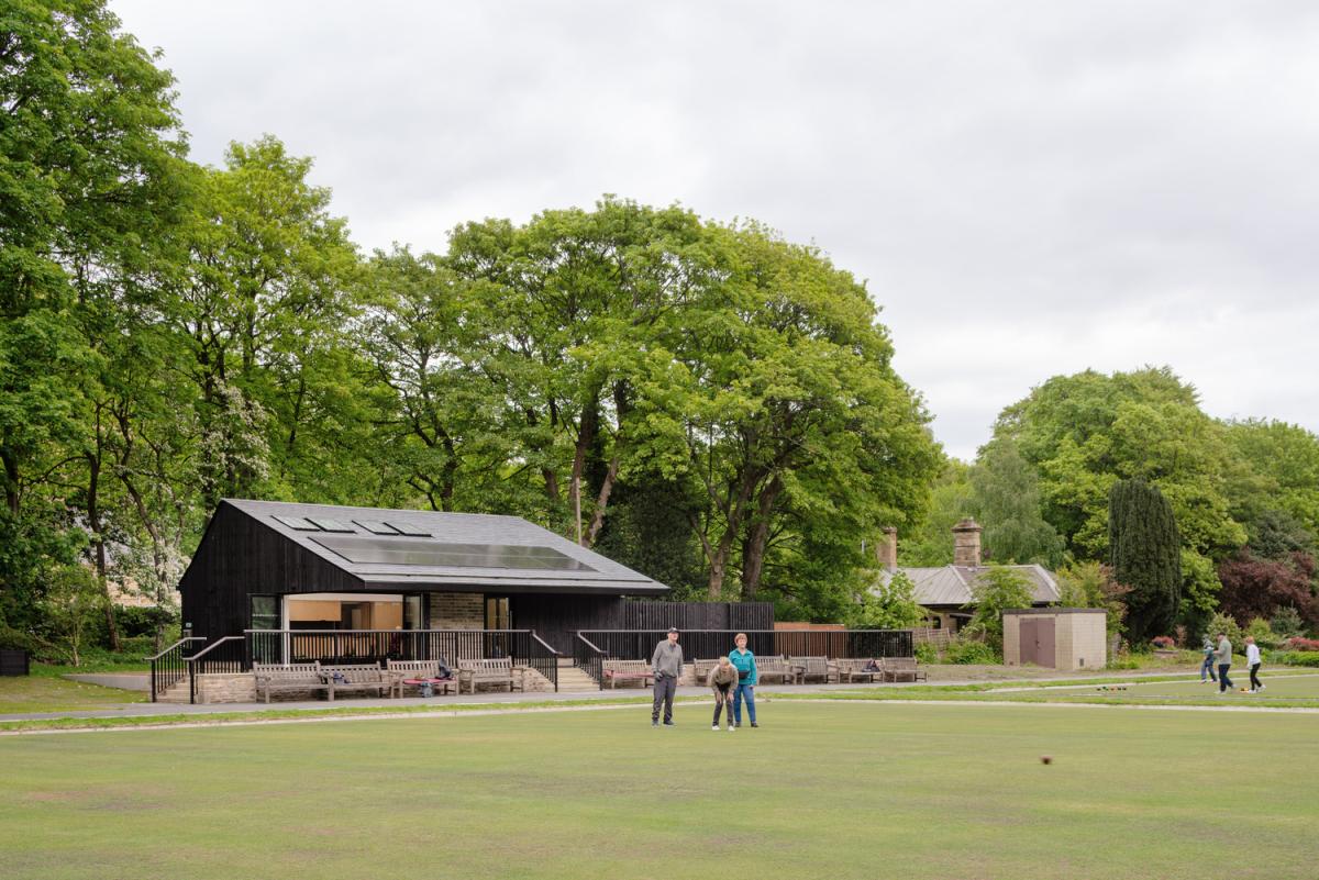 People playing crown green bowls on a green in a park setting, with a pavilion building behind.