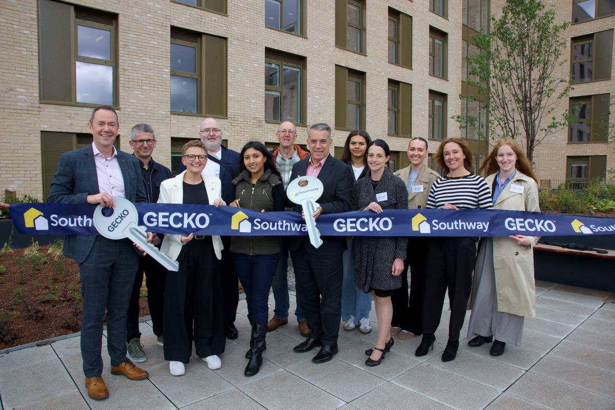 A group of people with a ribbon tape and over-sized keys outside new apartments.