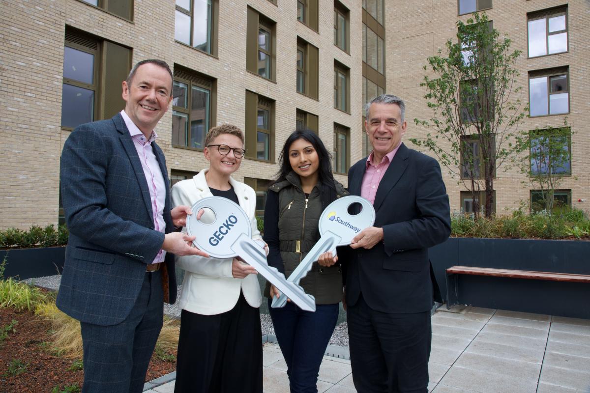 People smiling for a photo with over-sized keys outside an apartment block