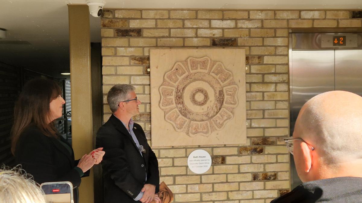 A heritage plaque unveiled on a wall of a new apartment block with people standing close by.
