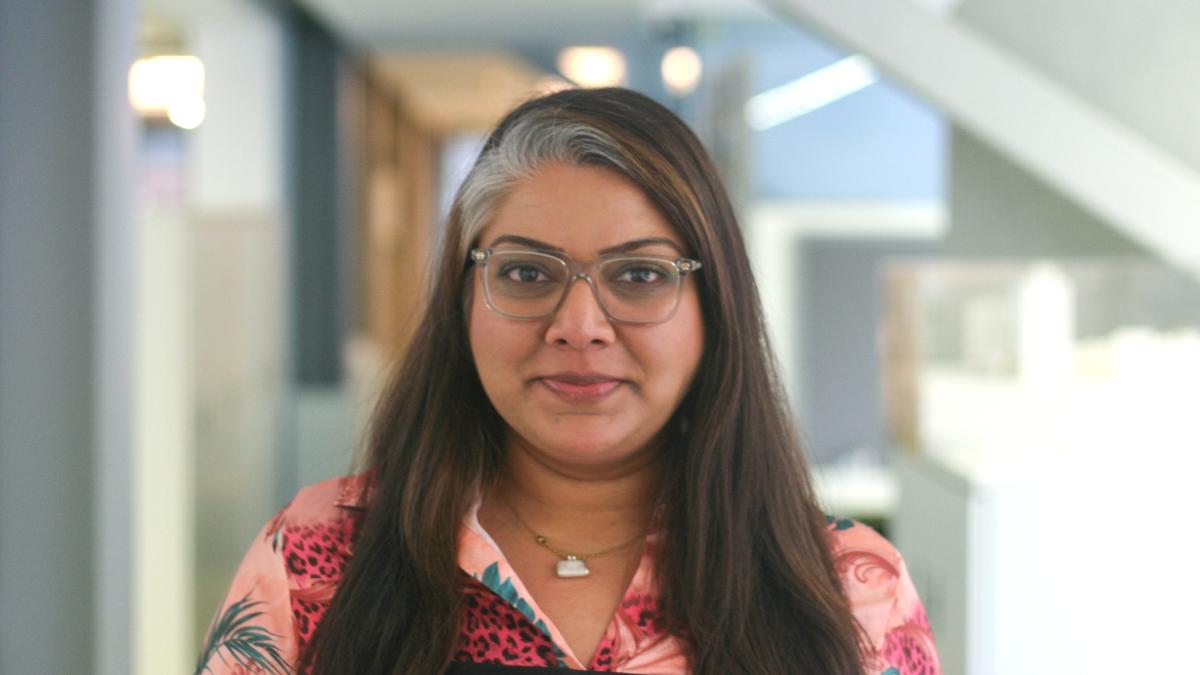Woman with black long hair, wearing glasses and a pink shirt.