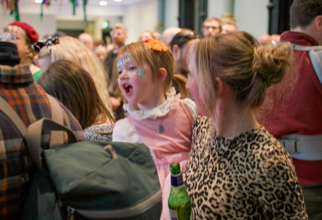 A little girl in her mothers arms are dancing in a crowd of people at Stretford Public Hall