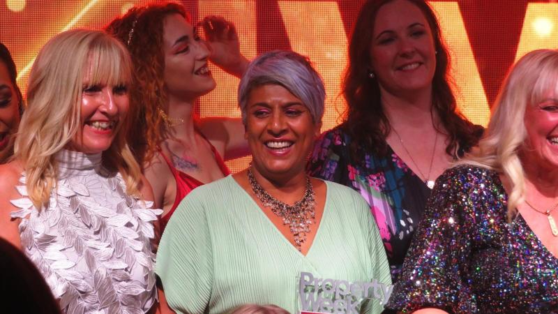 Image of women standing to receive applause at the end of an awards event. Chithra is centre in the image, smiling and holding her award. 