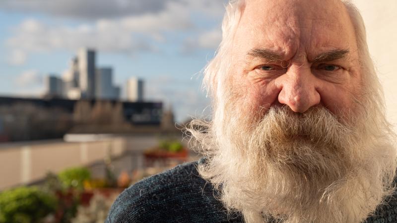 a portrait of man with large white beard with a city skyline as his backdrop