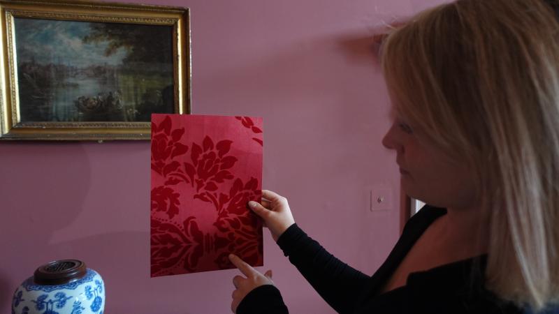 Hannah Bellerby, a woman with blonde hair, holding a piece of red wallpaper