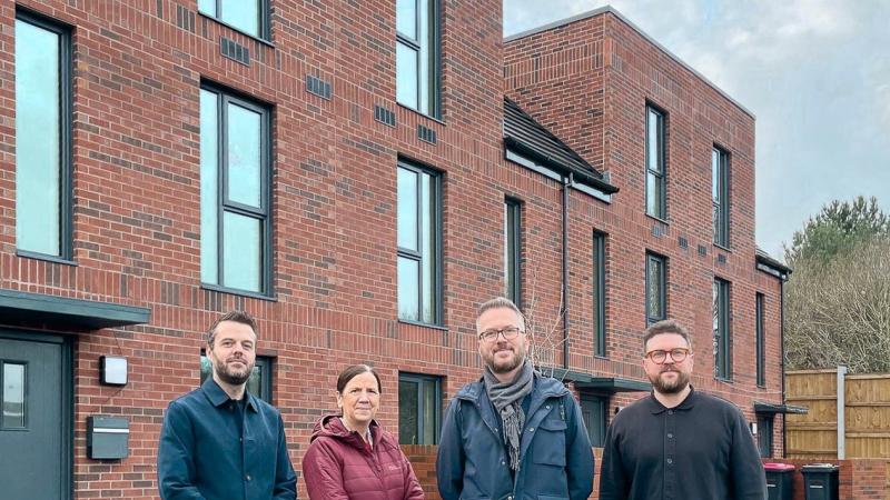 Four people standing outside a red brick house