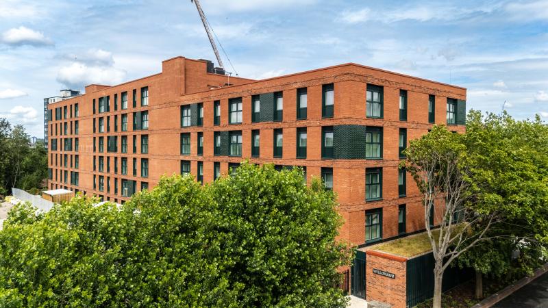 An aerial shot of a red brick apartment block building, surrounded by greenery.