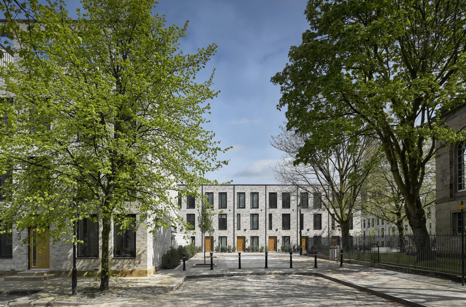 trees frame a square of grey brick townhouses on a sunny day