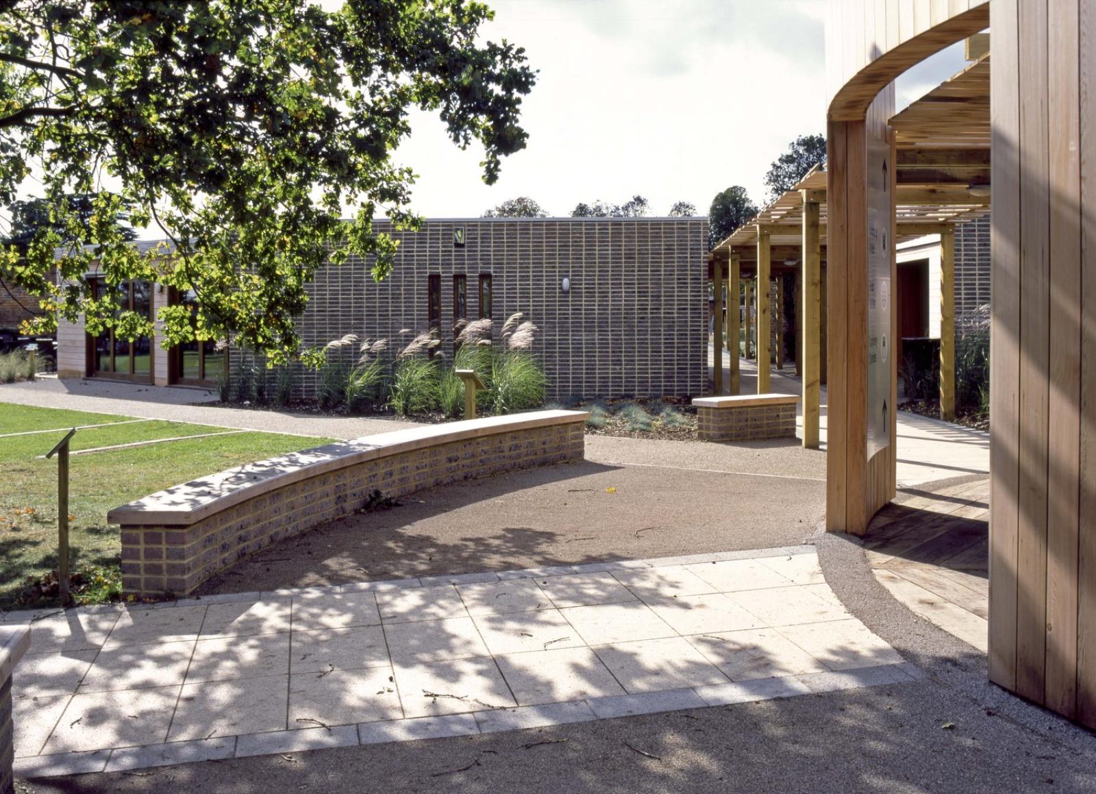 External image of a landscaped lawn and tree and seating areas infront of a timber walkway and welcome centre. 