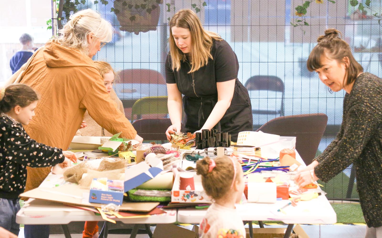 A group of women and children are working around a large craft table