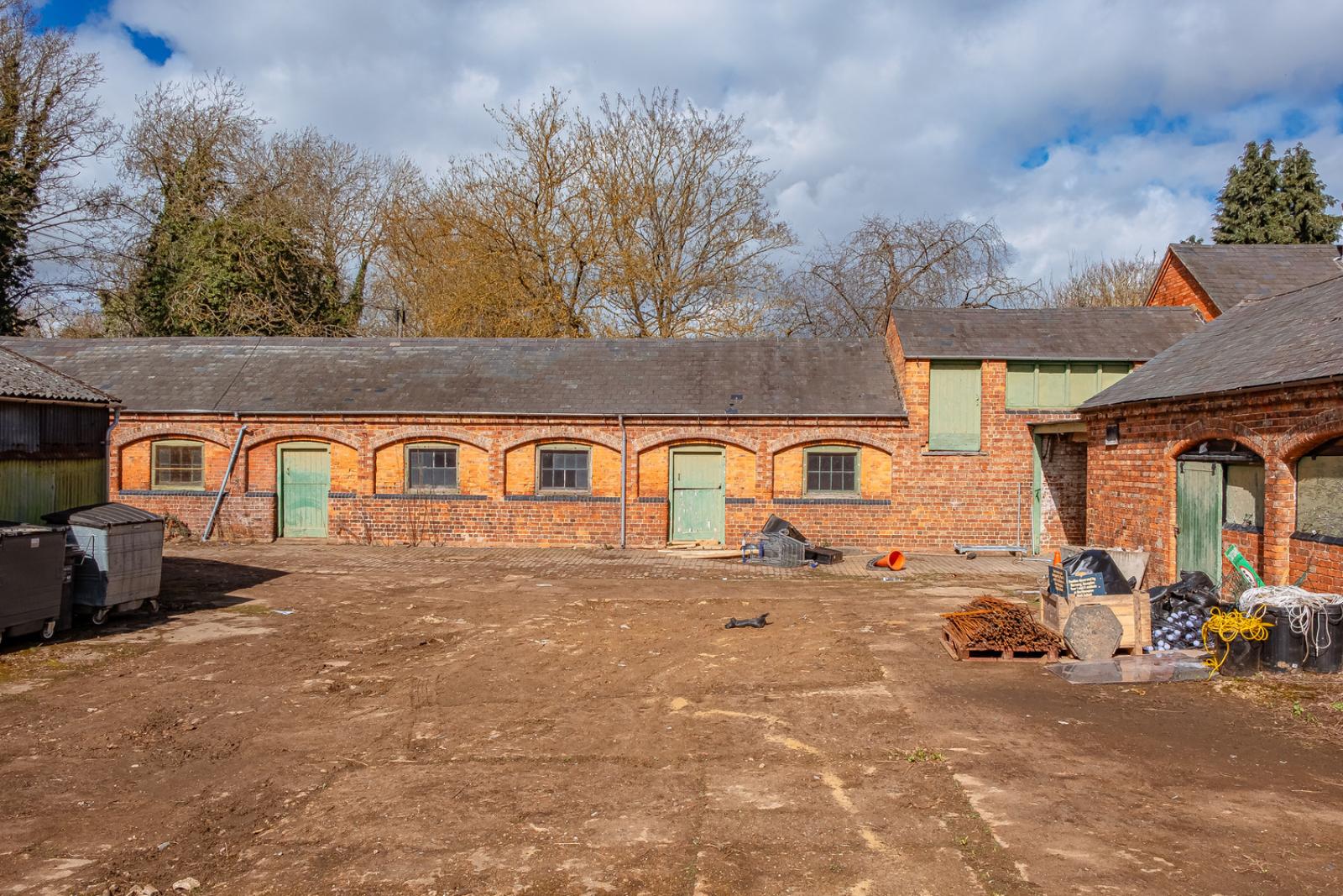 Delapre Abbey Stables pre-construction. Orange brick one-storey building with green doors.