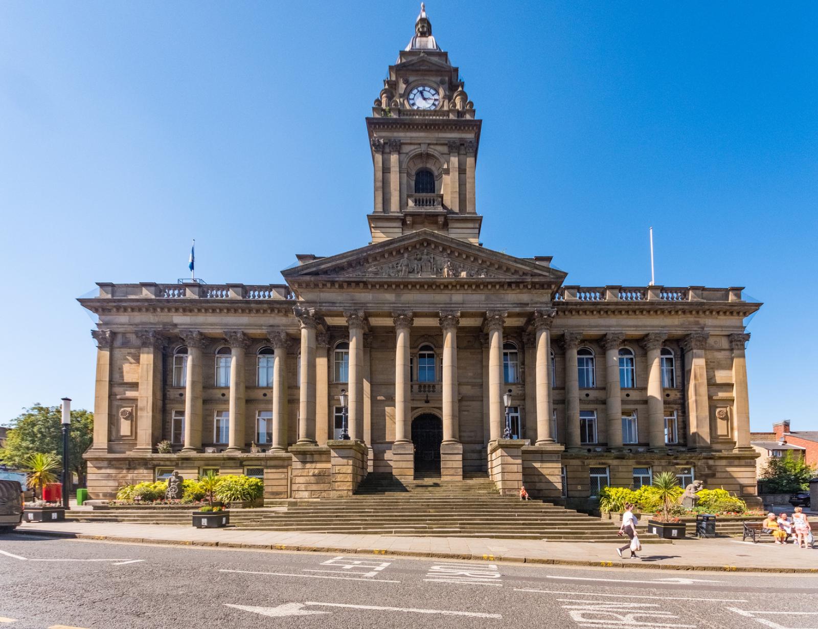 Morley Town Hall building. A dark brown stone building with columns and a clock tower