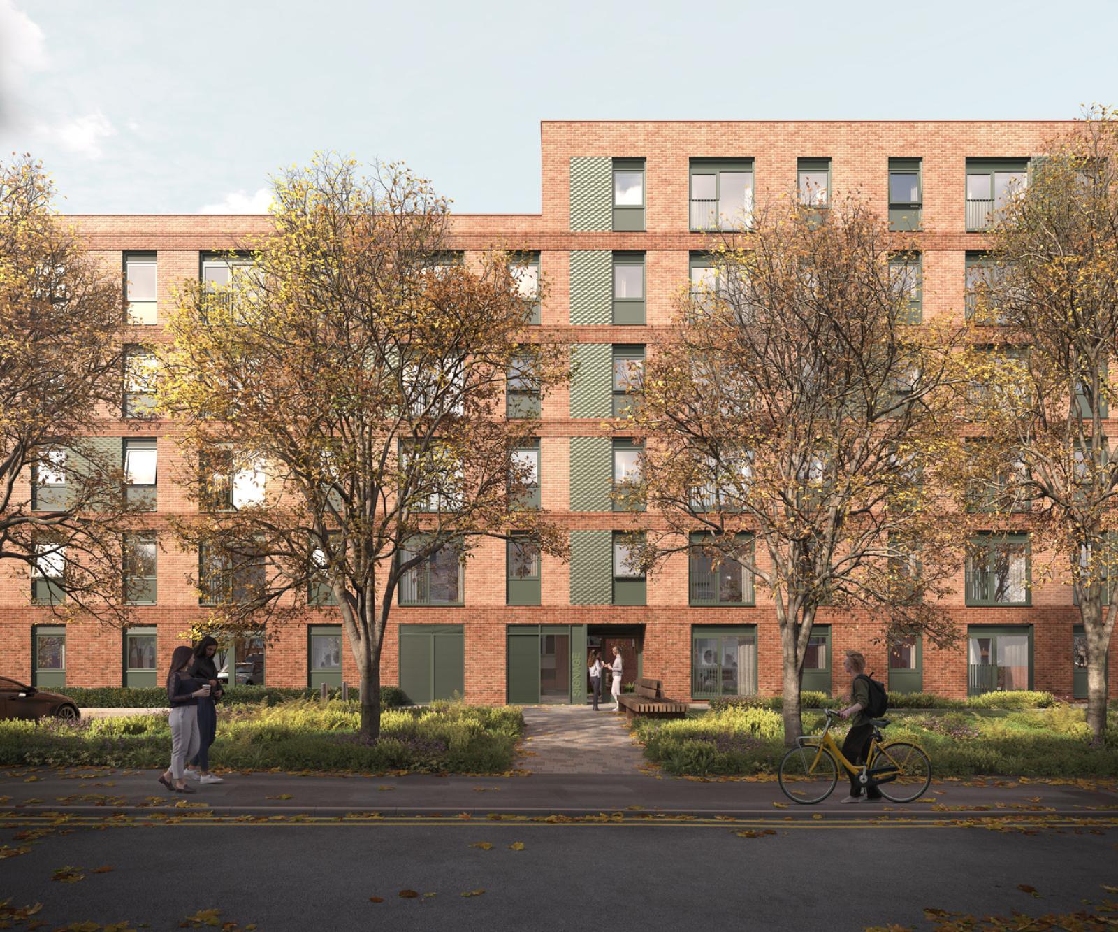 A block of red brick apartments up to five stories high, with windows. Trees and greenery outside with a pavement and people passing by.