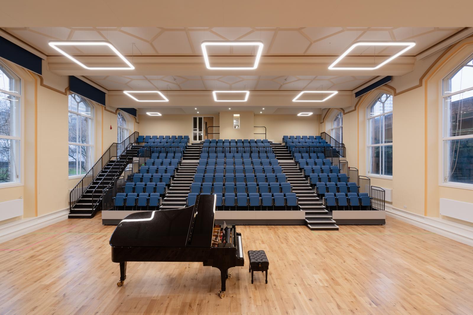 Whiteley Hall - a performance space with a piano in the centre of the room and blue tiered seating