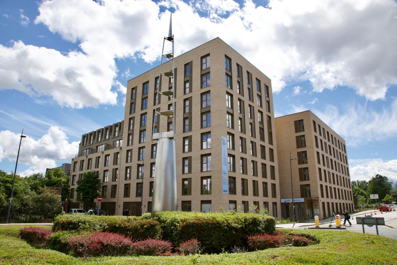 A large multi-storey residential apartment block with a green roundabout in front