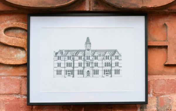 a pencil drawing of ancoats dispensary in a black frame in front of a brick wall