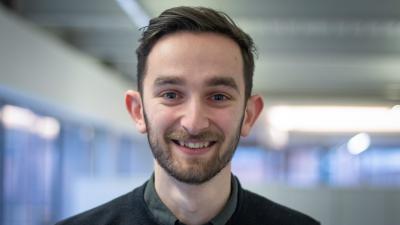 Headshot of Adam Lewis. A person smiling wearing a black jumper.