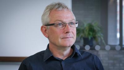 Headshot of Chris Whelan. A smiling man wearing glasses and a navy blue shirt.