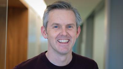 Headshot of David Coulson. A man smiling, wearing a maroon jumper.