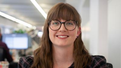 Headshot of Emily Green. A woman smiling, wearing glasses and a tartan print blouse.