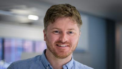 Headshot of Grant Prescott. A man smiling wearing a blue shirt.